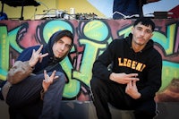 two young men posing for a photo in front of graffiti