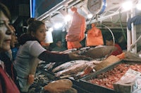 a woman is standing in front of a fish market