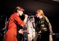 two women singing into microphones on stage